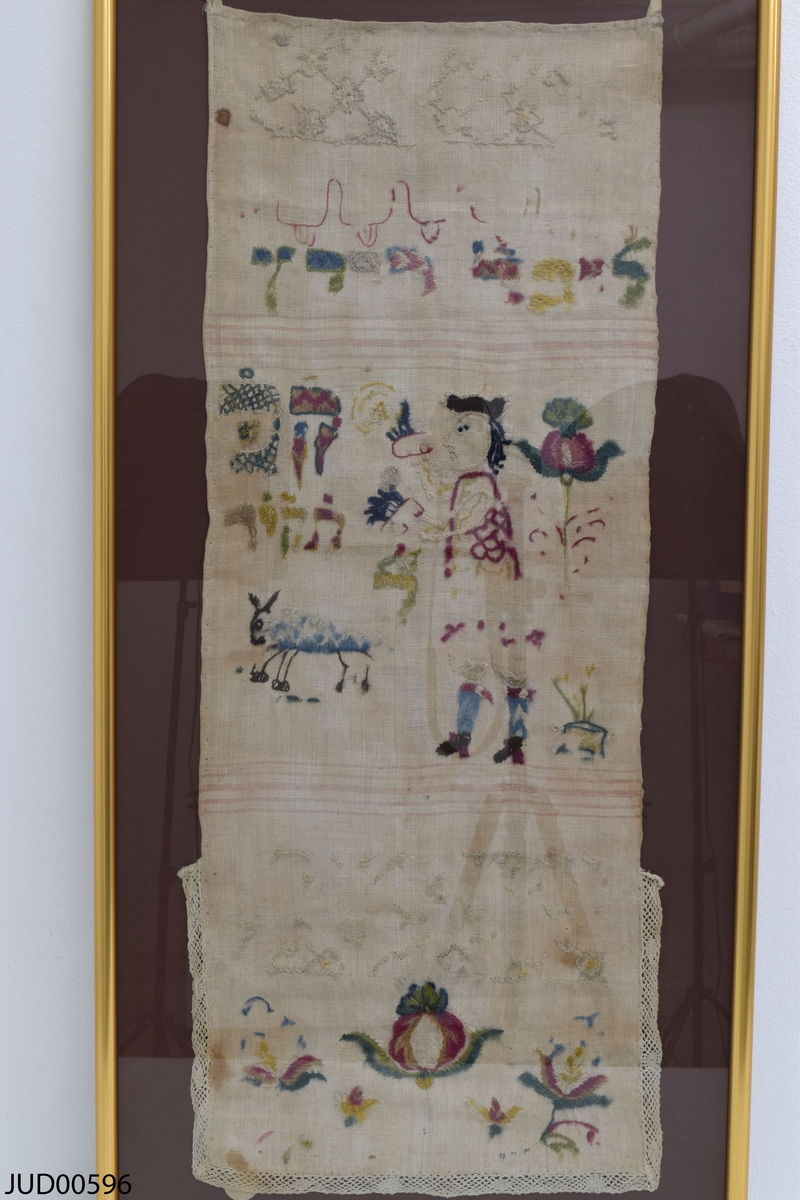 Bomullstextil med garnbroderi i form av figurer och hebreisk text. Har troligtvis använts som torahförhänge.