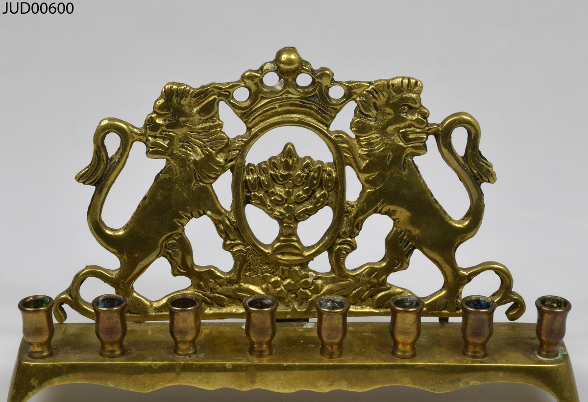 Gjuten mässingsljusstake med åtta ljushållare. Ryggen är dekorerad med menora flankerad av två lejon.