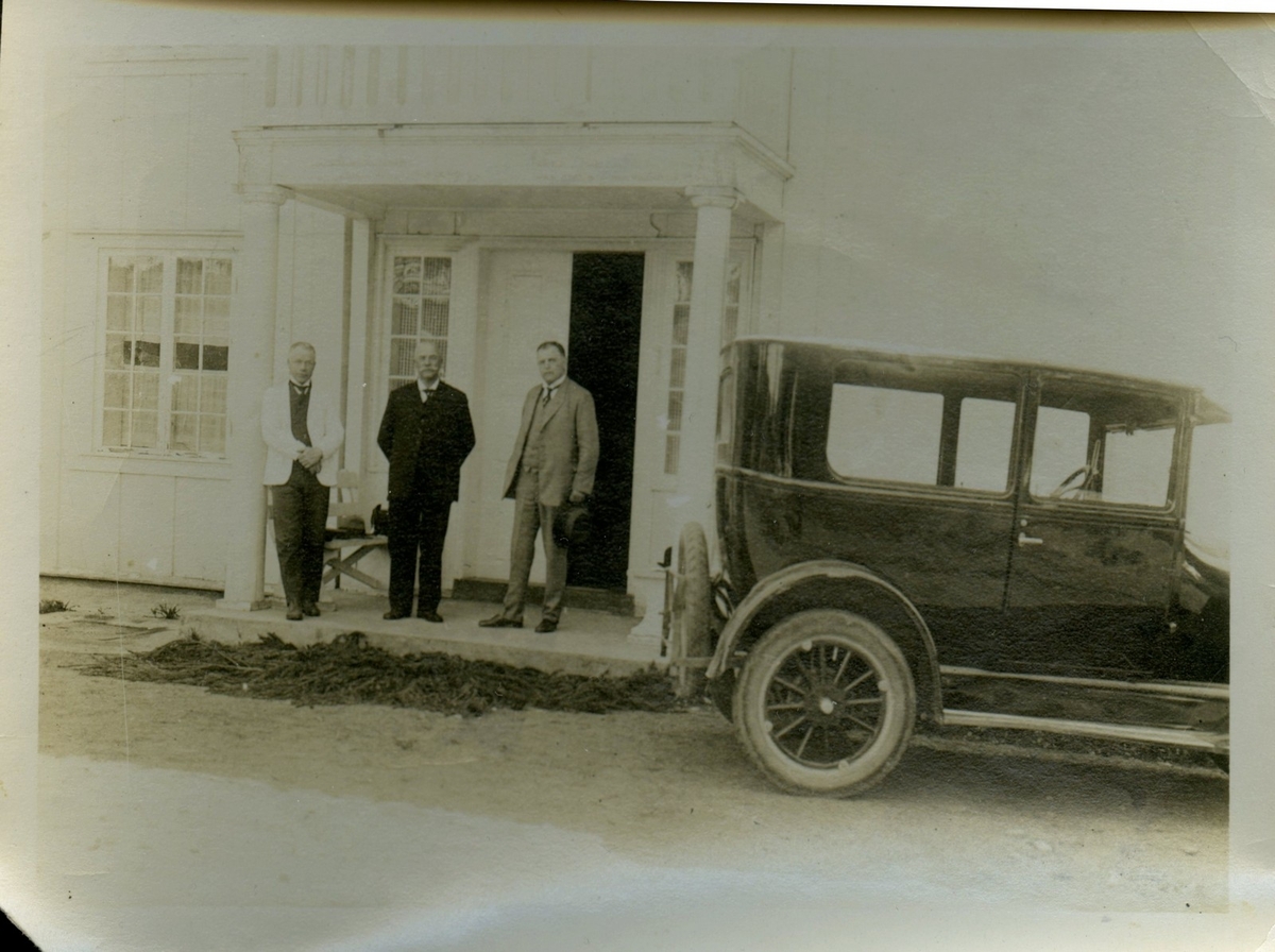 Fotografi av tre menn utanfor ein prestegard. Den eine av mennene er diktarpresten Anders Hovden, som på dette tidspunktet var prest i Østre Toten. Bilen på biletet tilhøyrer prestegarden. Fotografen er ukjend. På baksida av fotoet står datoen 7. juni 1926.