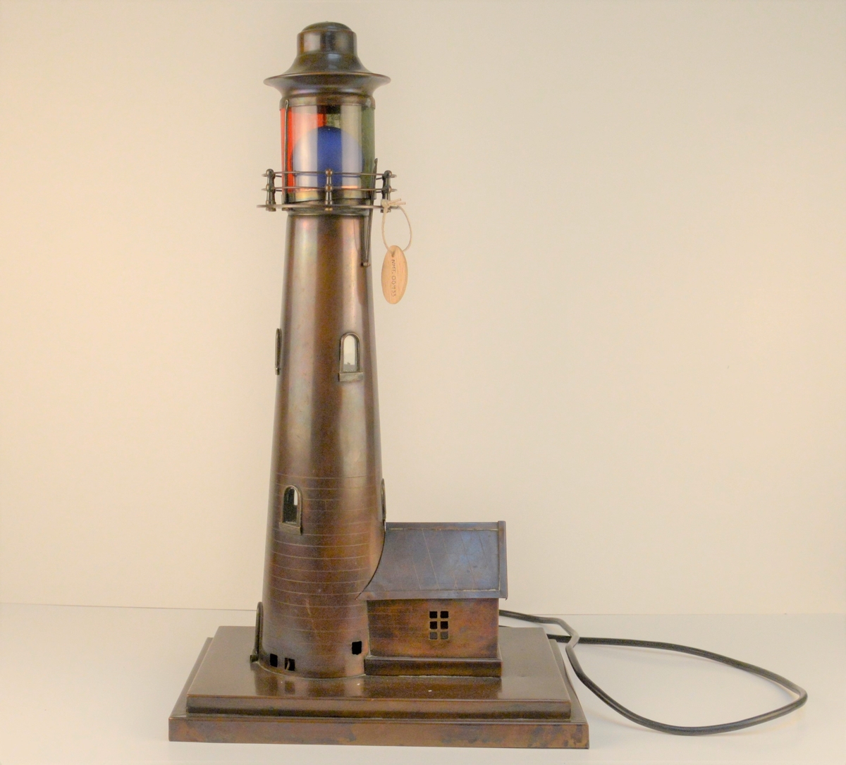 Modell av eit fyrtårn med blå lyspære i toppen og elektrisk ledning.