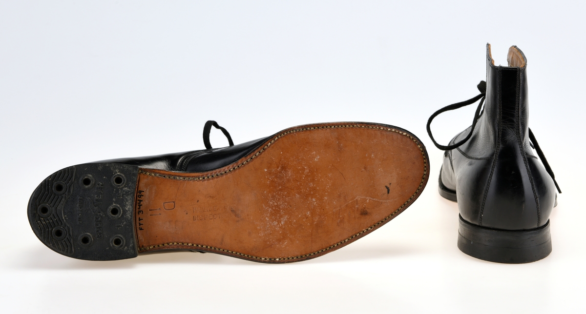 Et par høyskaftede herresko i størrelse 11 produsert av Stone-Tarlow. Skoene er sydd av svart skinn. Foran er de avrundet spiss. I front er det 10 par snørehull. Det er svarte metallmaljer på baksiden av snørehullene. Skoene er snøret med svarte, flate skolisser. Under snøringen er det en tunge av svart skinn som er foret med tynt ullfor. Innvendig er skoene foret med gråhvittt lerretsstoff. Det er innersåle av lyst brunt lær. Langs kanten oppe og kantene med snørehull er det også foret med lyst brunt skinn. På skoene er det dekor i form av stikninger. Skoene har yttersåle av brunt lær. Hælene har gummiflikk.