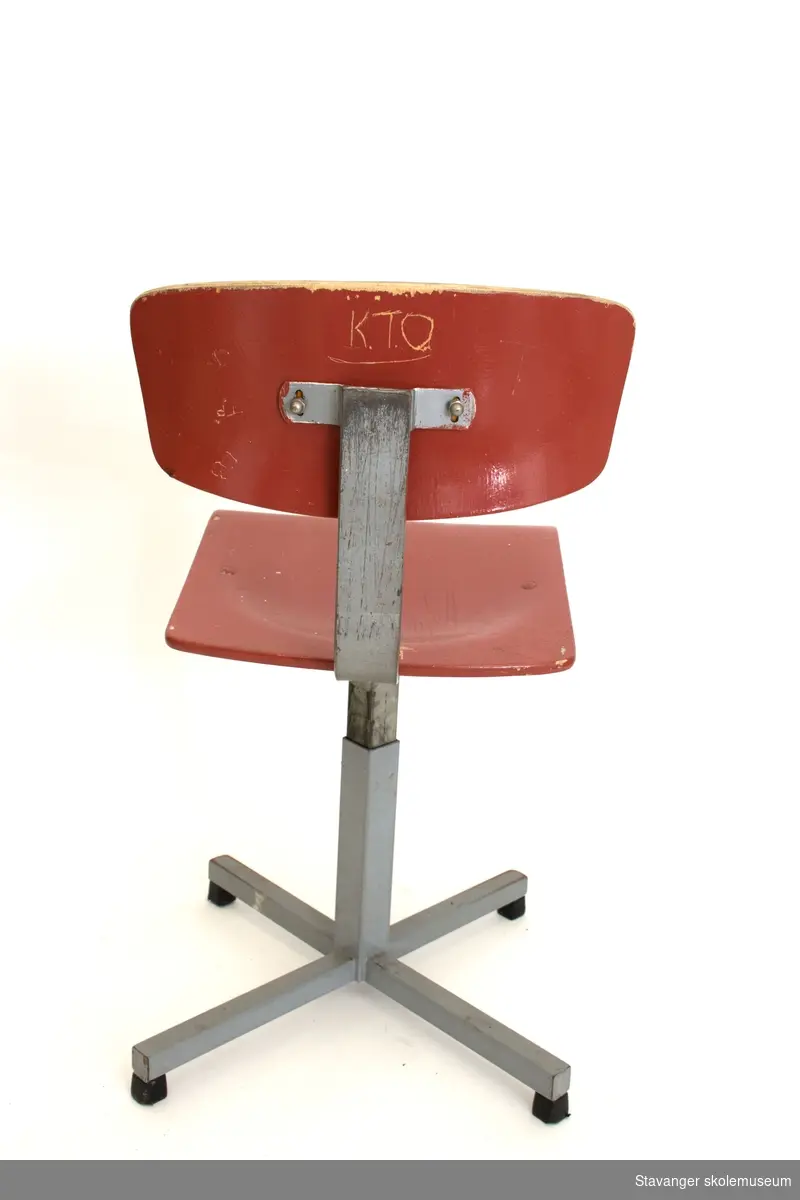 Elevstol av jern og bøyd kryssfiner. Gråmalt stål og rødmalt kryssfiner i sete og rygg. Er justerbar i høyde.
