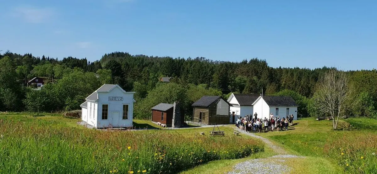 Oversiktsbilete av stor gruppe står samla nede i prærielandsbyen ein sommardag