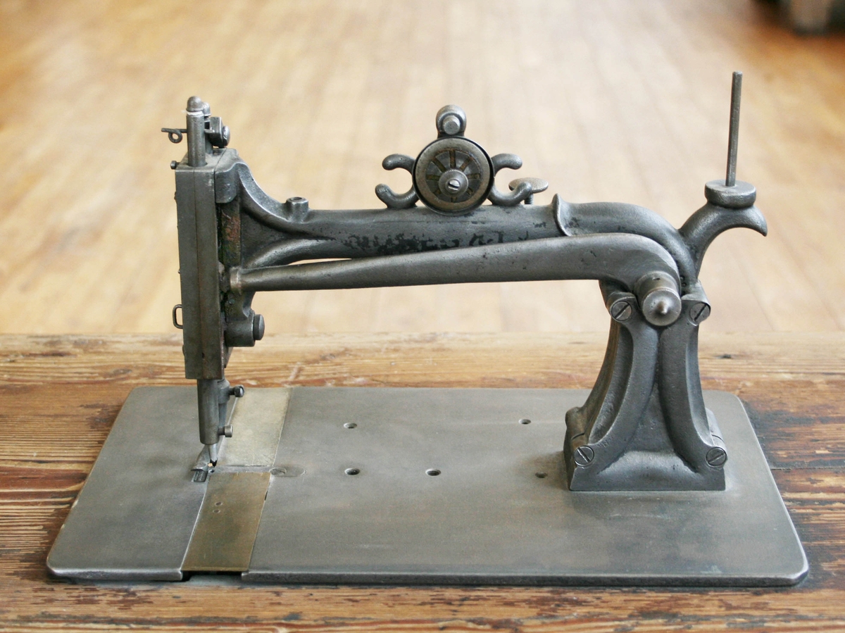 Symaskin i järn (omålad). Tillverkad av Jones Sewing Machine Co. Guide Bridge, Manchester, England. Monterad på rektangulär, trävit skiva av gran (ursprungligen troligen betsad). Står på omålat grått järnstativ med trampa märkt "HOWE". Långskyttel, remdrift.

Har tillhört Carl Hedberg, född 1846, död 1903, Långsered, Brunn. Symaskinen medfördes till de gårdar Carl arbetade.
