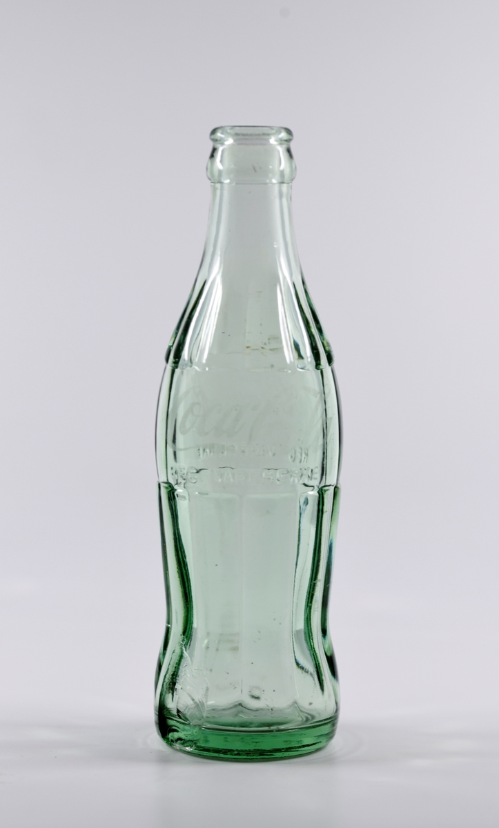 En sylinderformet Coca Cola-flaske støpt i lyst grønnlig glass. Flasken ble funnet under arkeologiske utgravninger i brønnen på Sverresborg Trøndelag Folkemuseum i perioden 2014-2016.