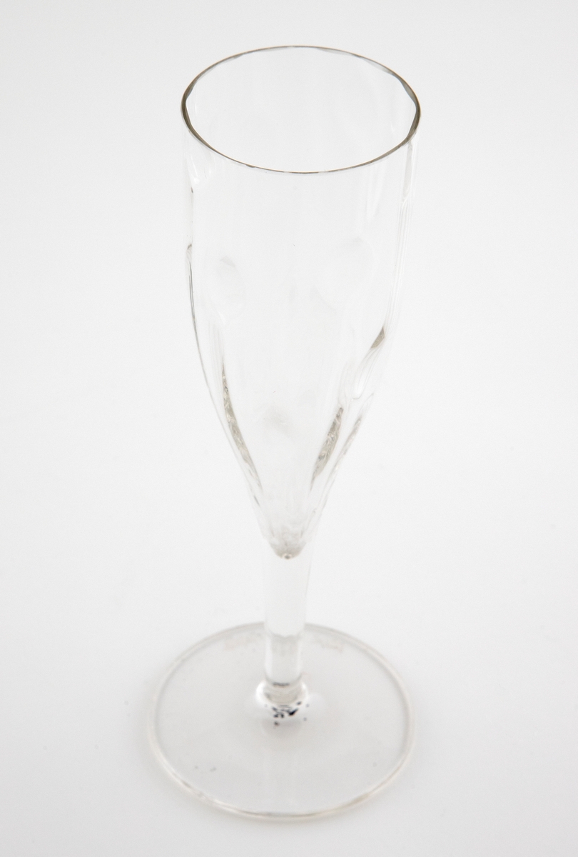 Champangeglass i klart glass. Konisk kupa som er dekorert med punktdekor. Hviler på en enkel stett og en flat sirkulær fotplate.