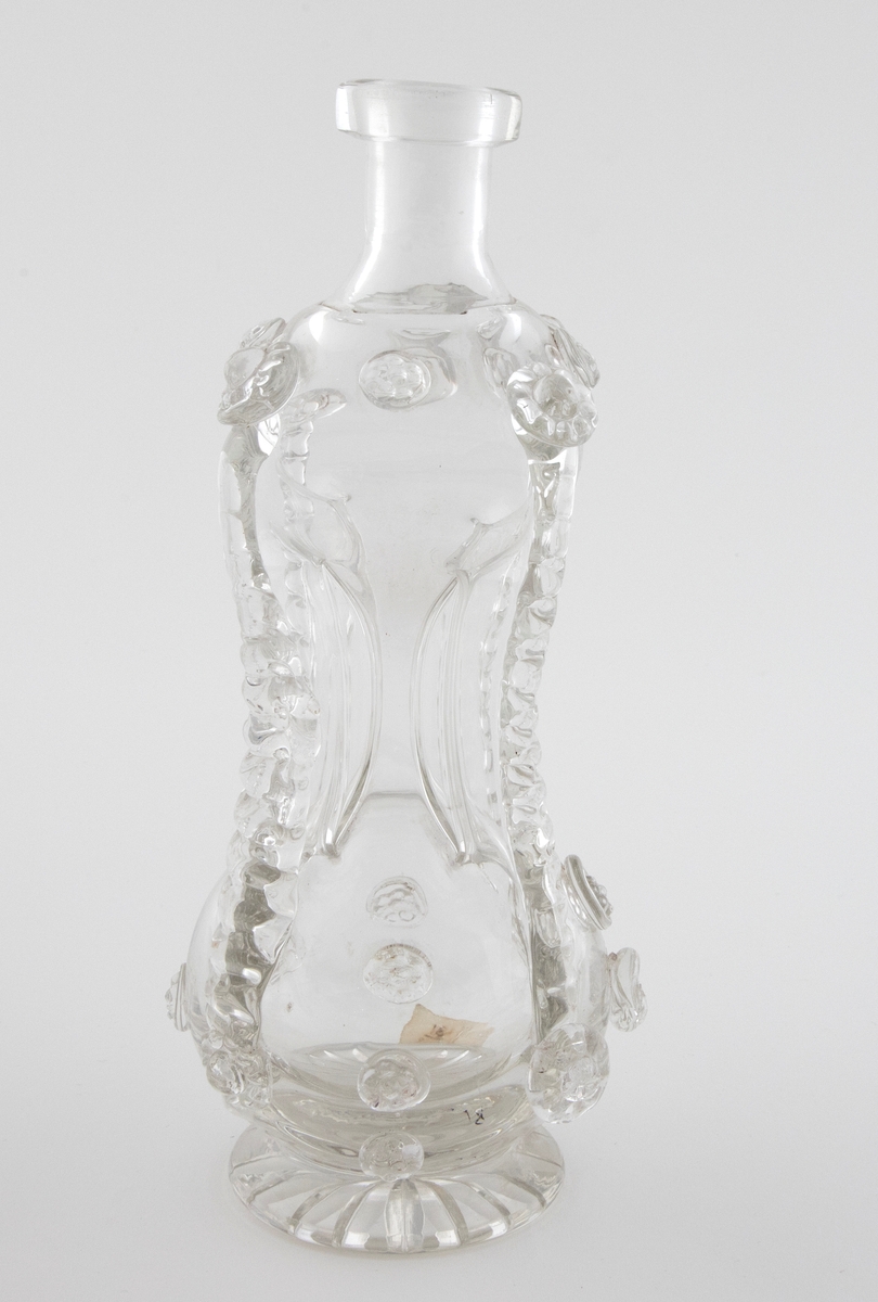 Timeglassformet klukkflaske i klart glass, hvor over- og underdelen er forbundet med et tynt rør. Korpus er dekorert med pålagte mønstre av strimler og "bringebær". Lav hals med glatt kantring, samt sirkulær fot med stjernesliping.