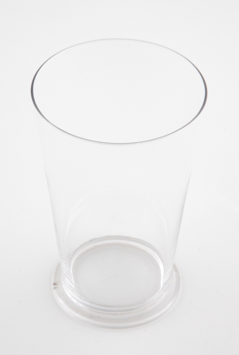 Tilnærmet sylinderformet drikkeglass med sirkulær fotring i klart glass.