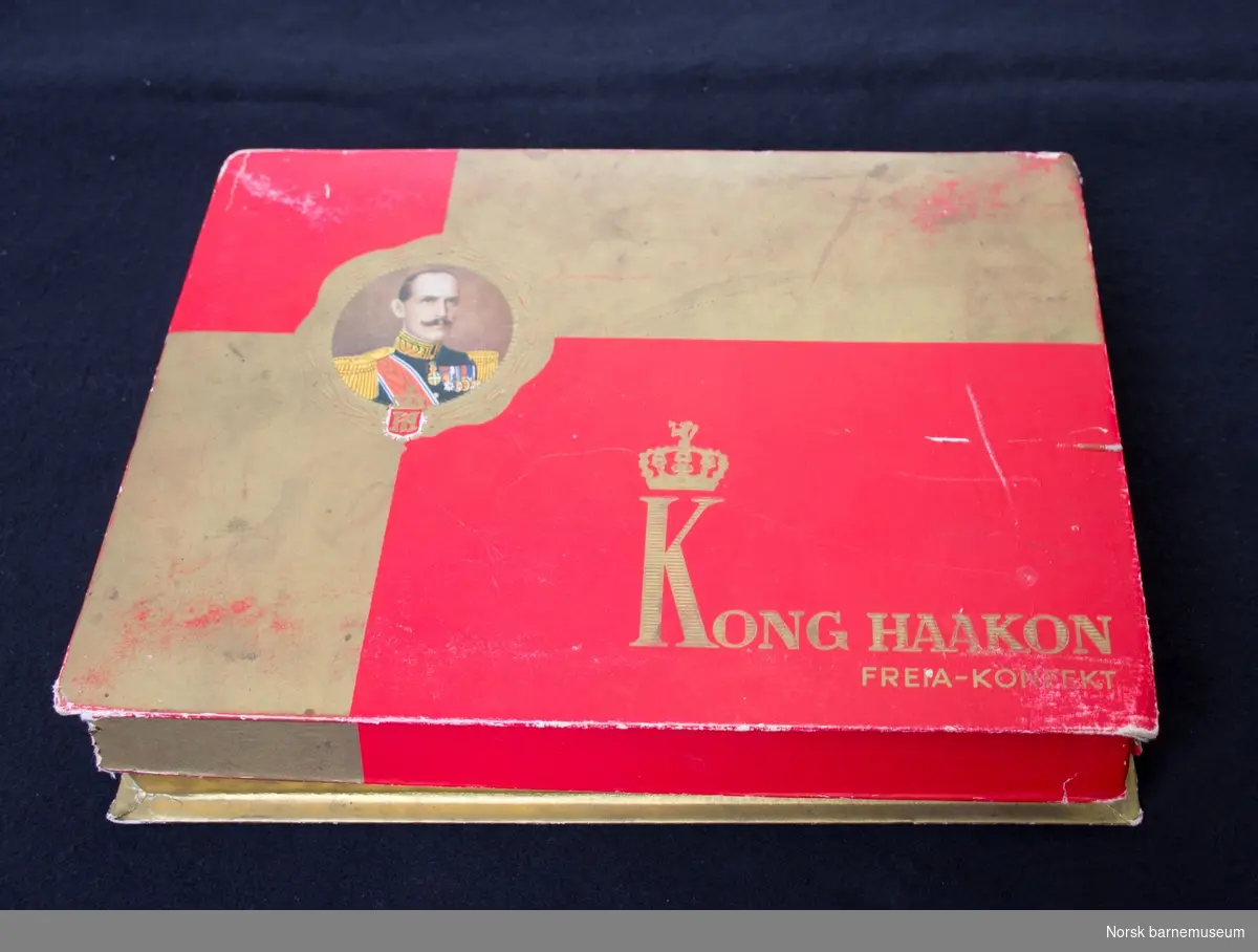 En samling papirdukker samlet i eske Kong Haakon, Freia-konfekt. 