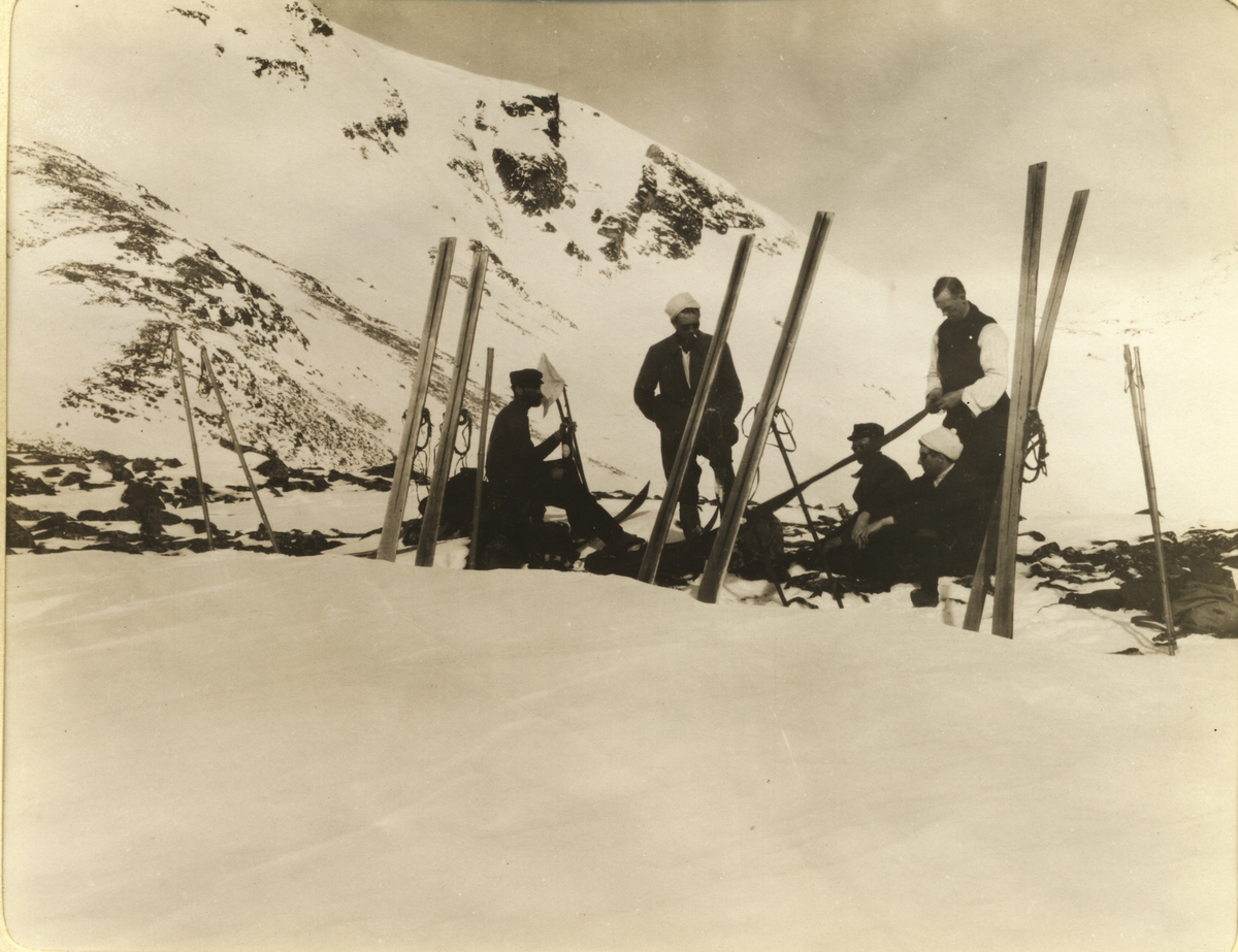 Fire skigåere raster ved Tjørnholet på vei til Glitterheim i Jotunheimen. Fotografert påsken 1910.