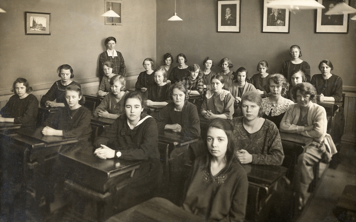 En skolklass sitter i sitt klassrum på Flickskolan, Växjö. Vid bortre väggen står deras lärare, Eva Lundgren.