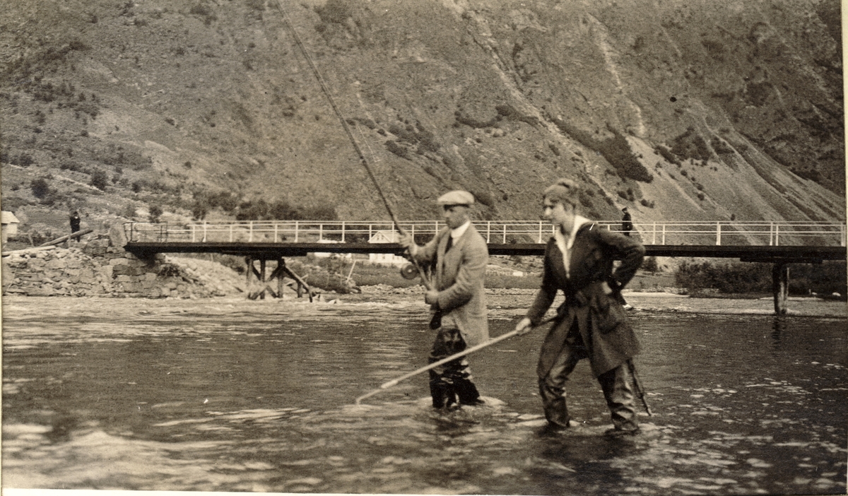 Westye P. Egeberg og søsteren Evelyn fisker i Lærdalselvi, Sogn og Fjordane. Evelyn står klar med klepp. I bakgrunnen bro over elven. Fotografert sommeren 1916.