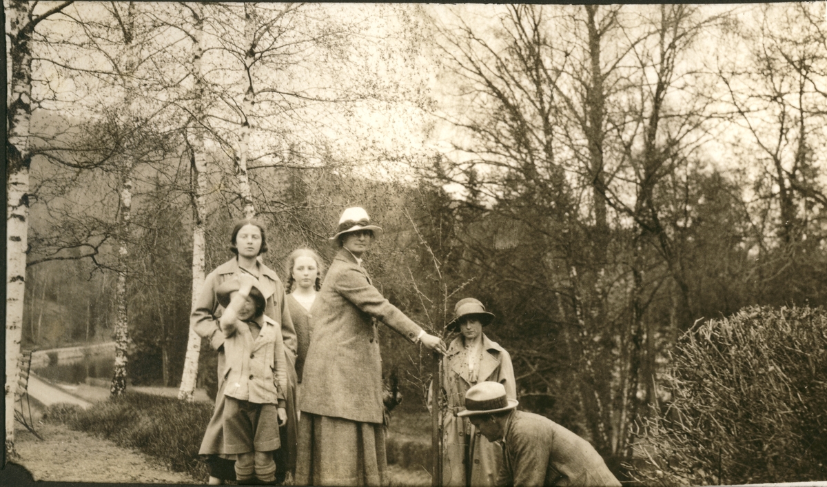 Nini Egeberg planter en bjørk med hjelp av gartner Anderson. Blant tilskuerne er antagelig de tre døtrene Mimi, Lucy og Karen. Fotografert på Bogstad gård 1924.