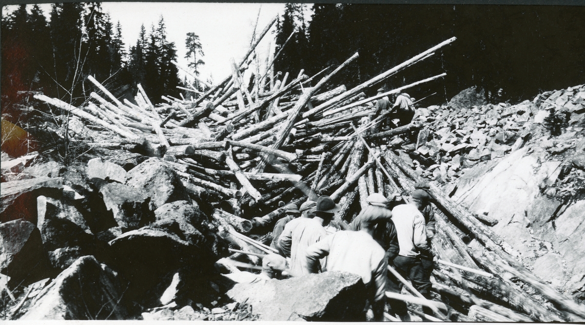 Opphopningen av tømmer(sætten) tørkes før dammen (Gaula dam i Melhus?) tas i bruk. Fem tømmerarbeidere står i forgrunnen. Fotografert 1928. 