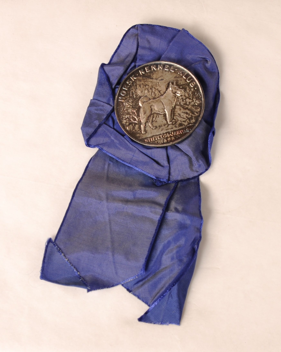 Rosett av blått tekstil med medalje av sølvfarget metall i midten