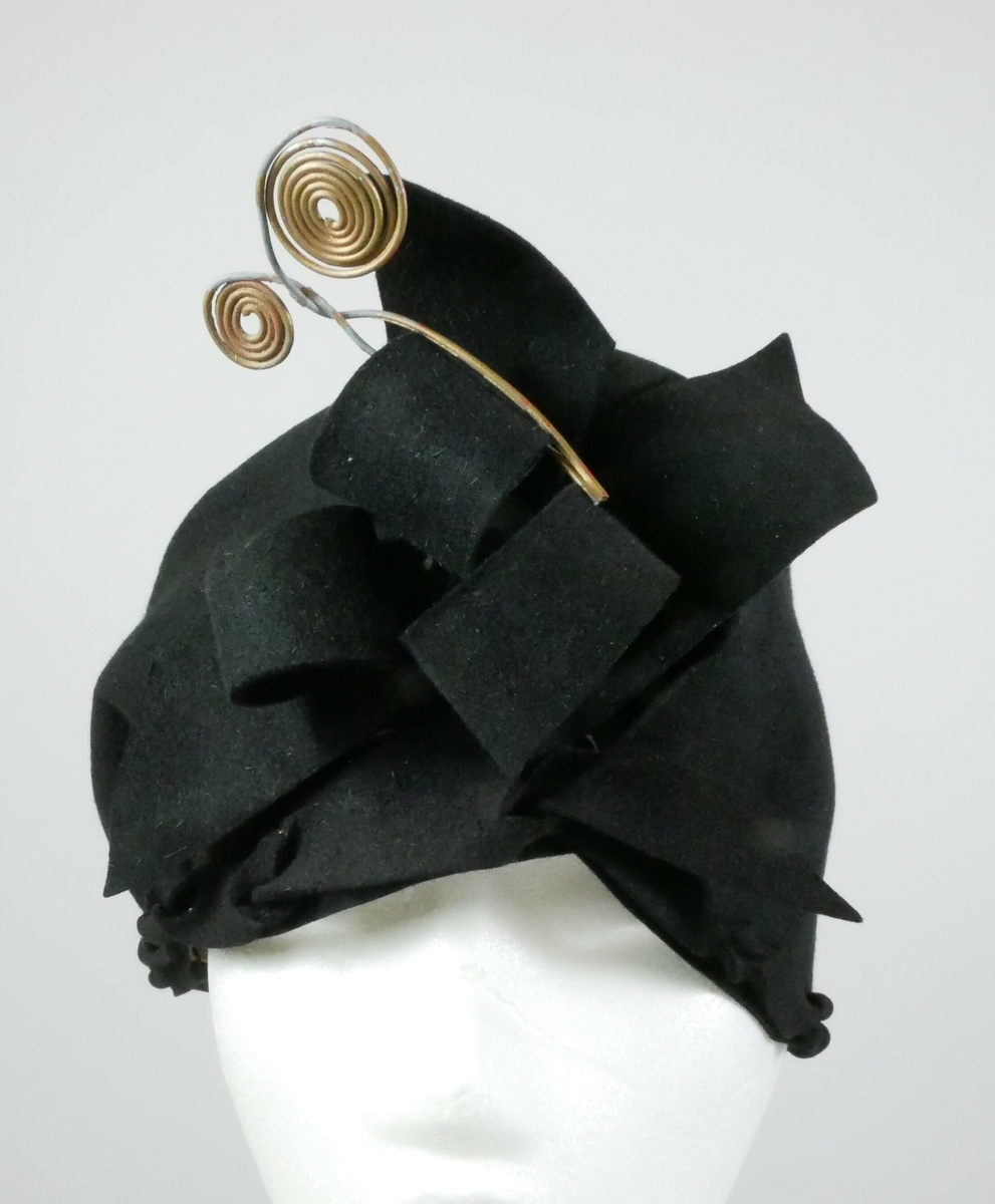 Svart hatt med dekorelementer foran i svart tekstil og metall. 