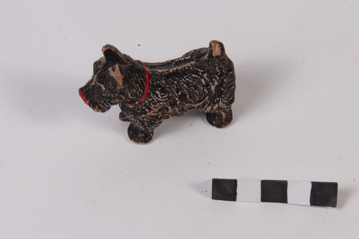 Svart lekehund av tre, med rødt halsband og rød nese.