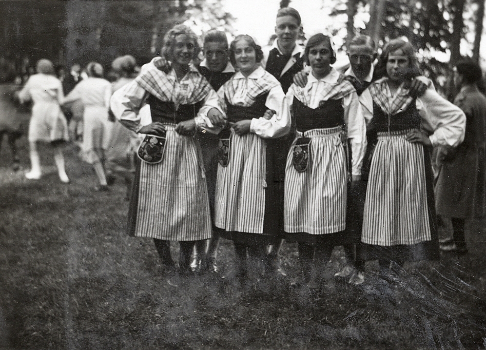 Några glada ungdomar i folkdräkt har ställt upp sig för fotografen. 
Text under fotot:" Danslaget i Boulognerskogen, midsommarafton 1931".