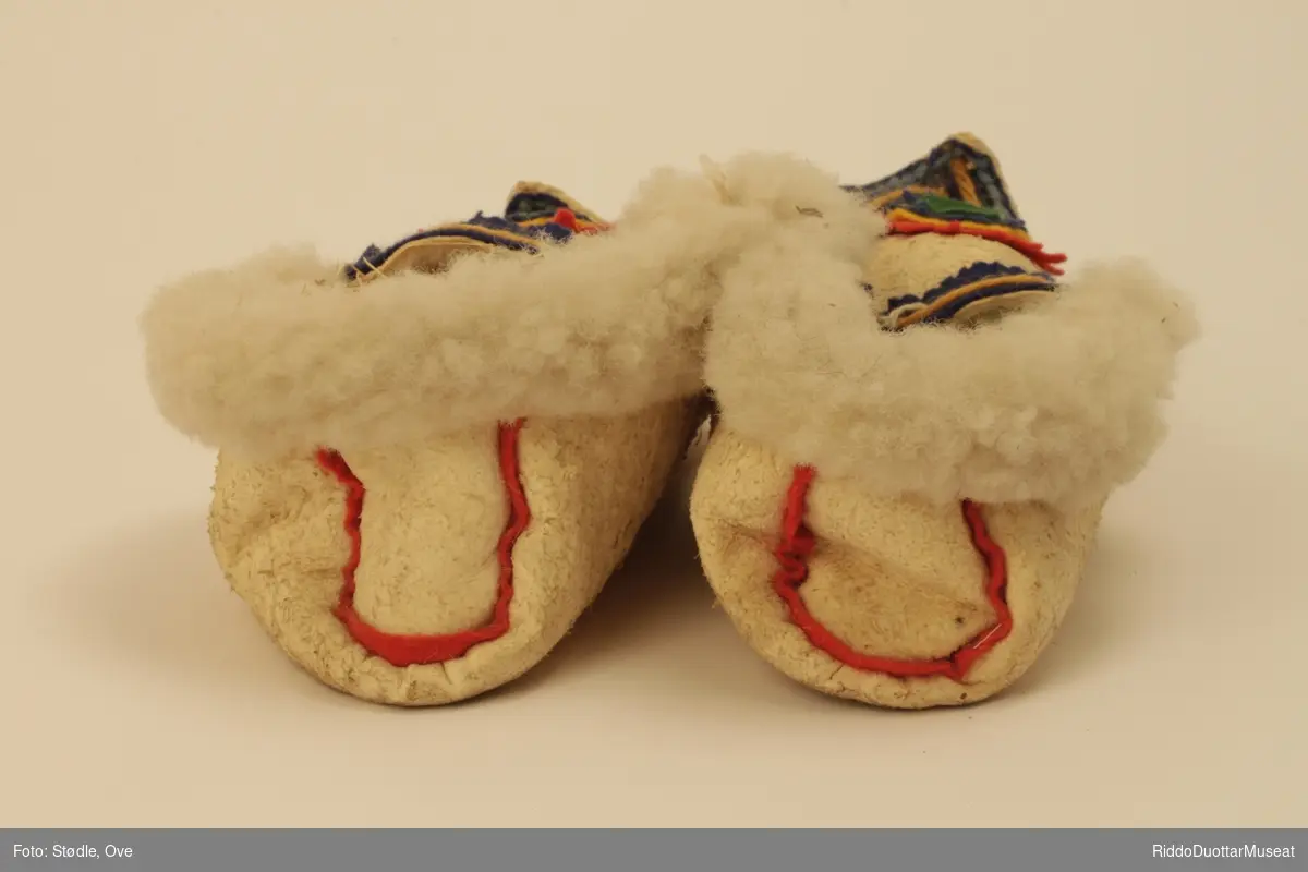 Tøfler av saueskinn sydd etter mal av tradisjonelle samiske skaller. Skinnet er vrangsydd med ulla inn, unntatt  brettekant som har har ulla ut.  Sømmene rundt overlær og helkappen har biser i ullklede. 