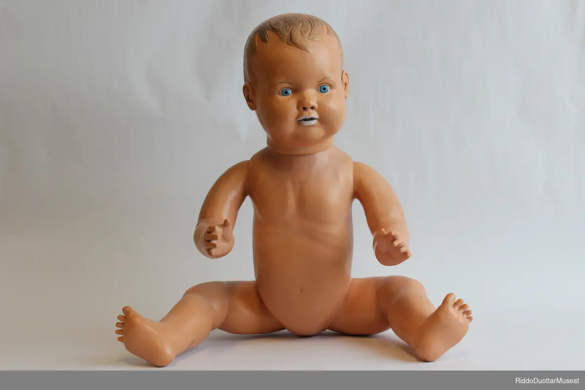 Hardplast dukke med bevegelige armer og bein. Hodet er tungt og faller bakover og til siden. Dukken skal blant annet kunne brukes til å lære hvordan man må holde babyens hode ved løft.