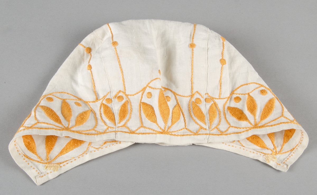 Mössa sydd av ett mittstycke med två sidostycken av vit linnelärft med broderi i plattsöm och stjälksöm av gul marcerisrérat bomullsgarn.