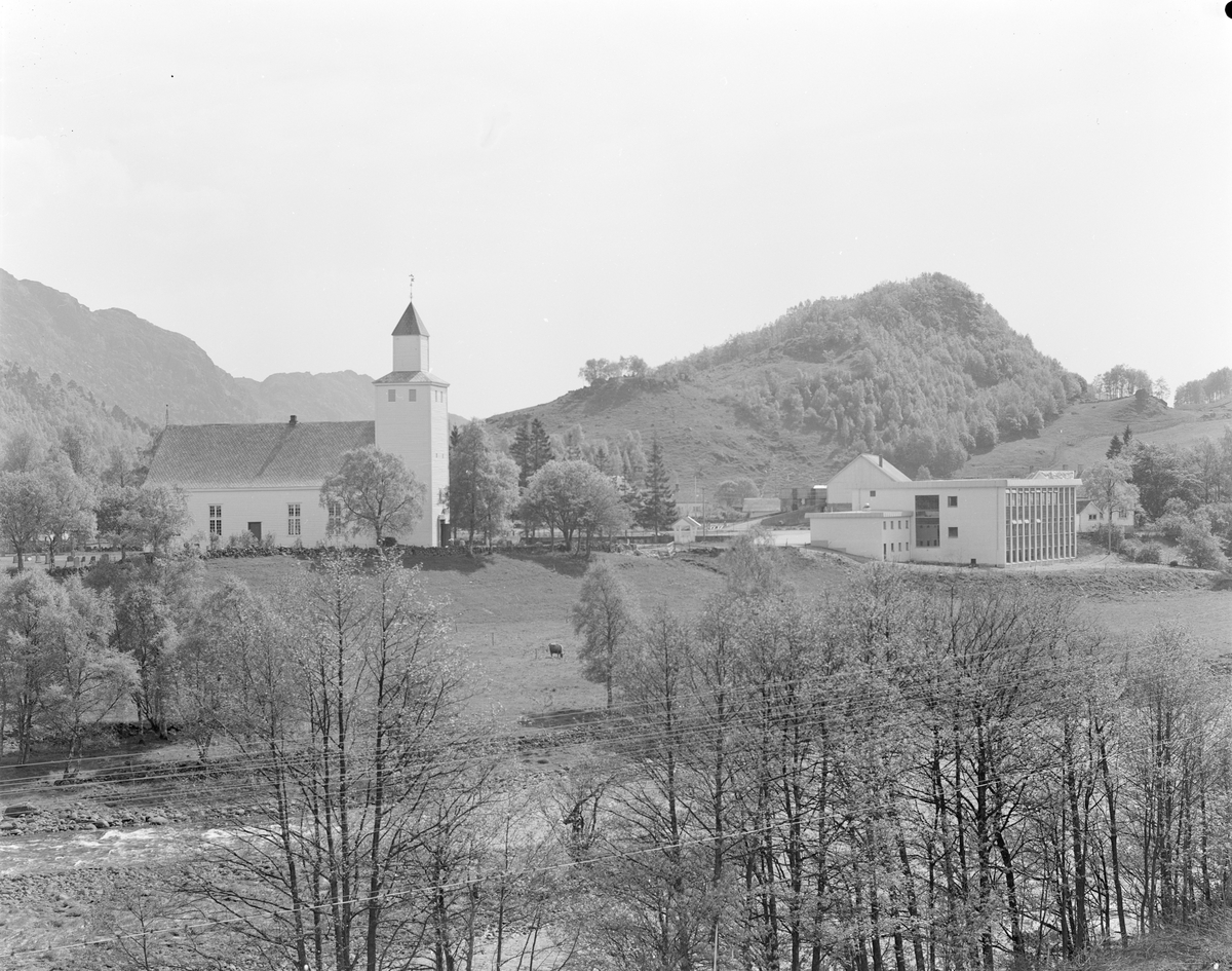 Bjerkreim kirke med Bjerkreim skule til høyre. I forgrunnen renner Bjerkreimselva og i bakgrunnen ligger Mæråsen. Nederst på det første bildet står det "Bjerkreim" og Enerett: Fotohuset."