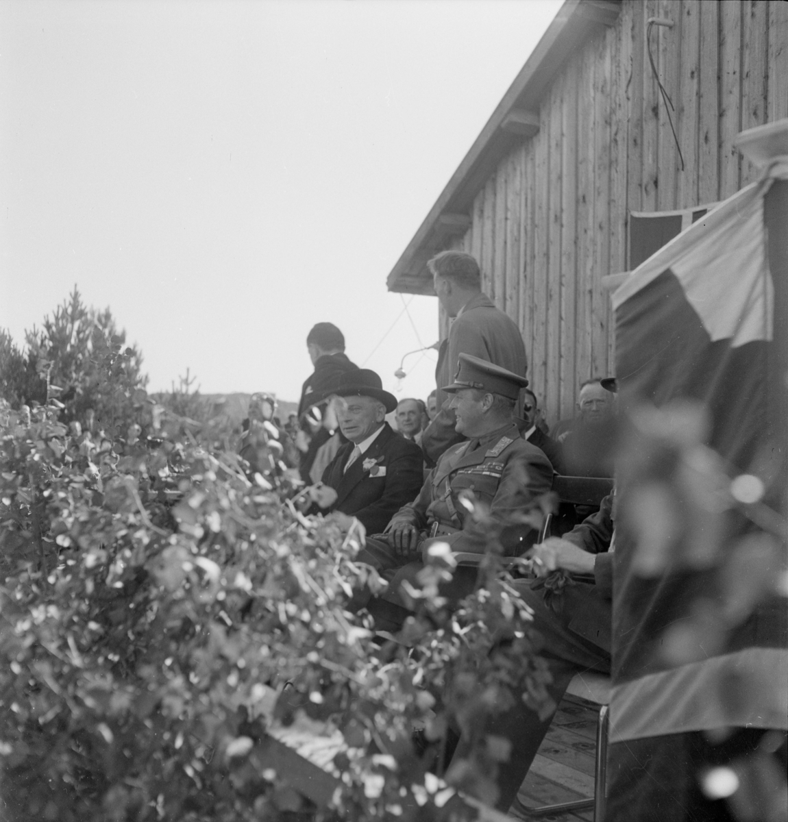 Menn sitter på rad og rekke bak talerstolen under åpningen av Eigerøy bru.