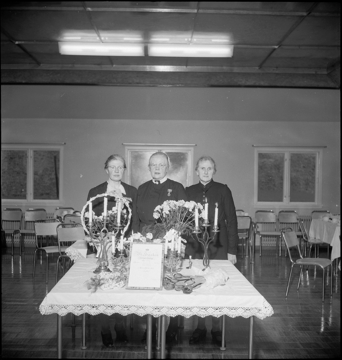 Et helselag samlet rundt en diplom fra kong Haakon. Kvinnen i midten har også en medalje. De er også samlet til kaffe.