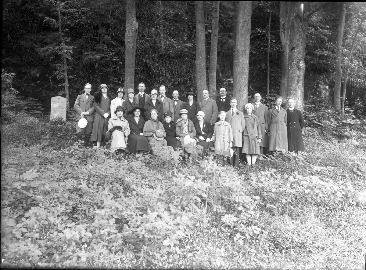 Gruppbild med män, kvinnor och barn sittande och stående intill en gravsten vid bergets fot på Gränna kyrkogård. Det är släkten Ekwall - en Röttlesläkt - som samlats vid Ekwalls familjegrav