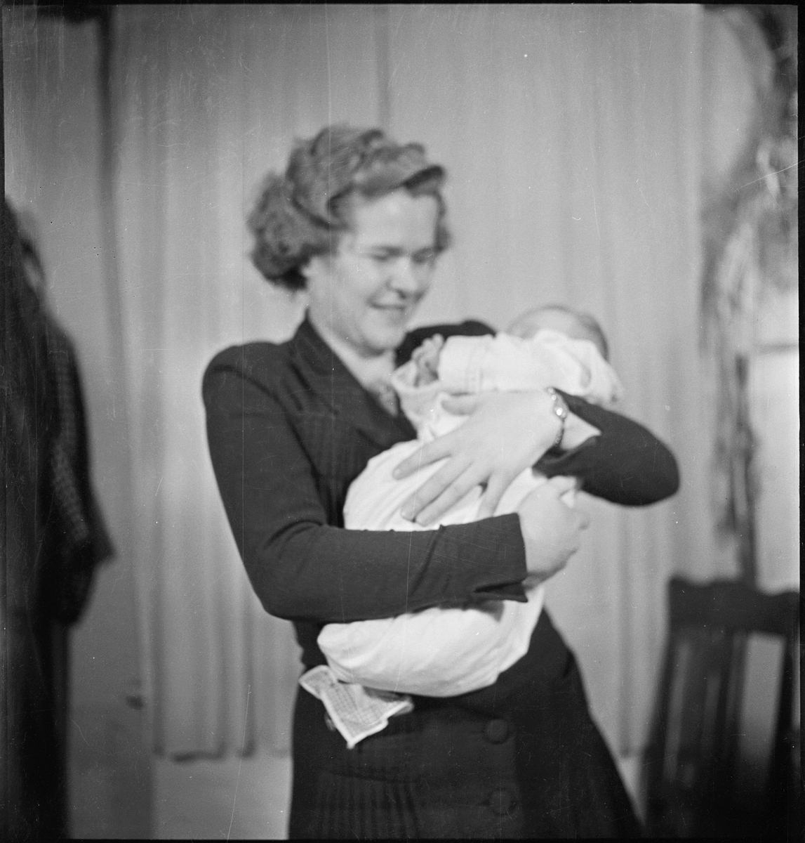 En kvinne med et nyfødt barn i armene. Bilde nr. 7 er av en barnepike med barnet i armene og bilde, 8 og 9 er av en stue med blomster og pynt i anledning den nyfødte.