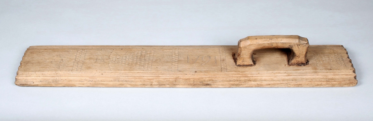 Mangelbräde i brunbetsat trä. Infällt, skuret handtag på ena änden. Avlång, med upphöjt mittparti och avfasade, profilerade kanter. Längs mitten, skuren dekor, i form av bårder med nagelsnitt samt årtalet "1791". Kortsidorna också med nagelsnitt. 

Mangelbräde eller kavelbräde är ett redskap av trä som använts för mangling av textilier. Mangelbrädet användes tillsammans med en kavel, en slät rulle av trä. Den textil som skulle manglas, rullades upp på kaveln, på ett bord eller annat slätt underlag. Under hårt tryck, rullades kaveln med hjälp av mangelbrädet, fram och tillbaka över bordet. (Wikipedia)