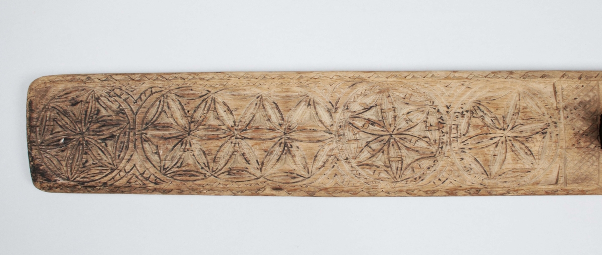 Mangelbräde i brunbetsat trä (färgslitage). På ena änden, infällt, skuret handtag (ej original). Brädet med skuren dekor, i form av 6 bladrosetter inom zig-zagbårder. Långsidor nedfasade. Närmast handtaget rektangulär ram med rutmönster. På ovansidan skuret: IAS ALO, 1747

Mangelbräde eller kavelbräde är ett redskap av trä som använts för mangling av textilier. Mangelbrädet användes tillsammans med en kavel, en slät rulle av trä. Den textil som skulle manglas, rullades upp på kaveln, på ett bord eller annat slätt underlag. Under hårt tryck, rullades kaveln med hjälp av mangelbrädet, fram och tillbaka över bordet. (Wikipedia)