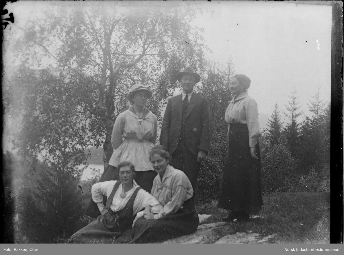 Fire kvinner og en mann oppstilt utendørs. To av kvinnene sittende på bakken.