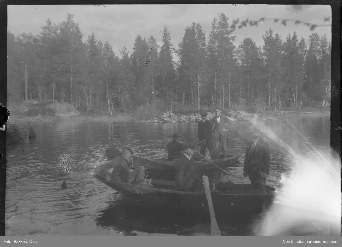 Gutter og menn stående og sittende i to robåter på vann.