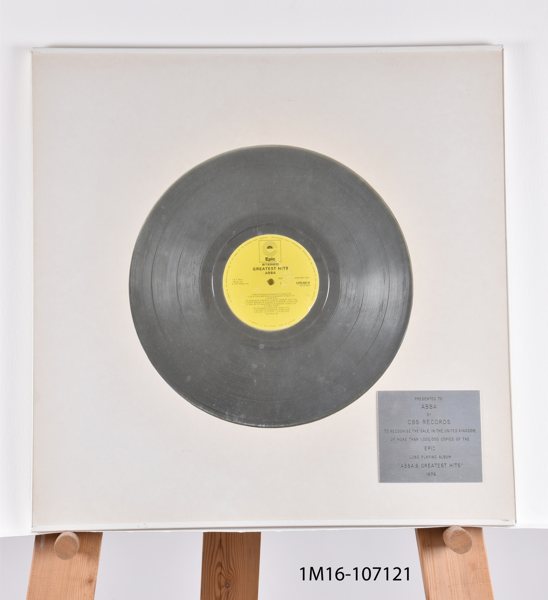 Guldskiva utfärdat till ABBA av CBS Records för mer än 1 000 000 sålda exemplar av ABBA Greatest Hits. Silverfärgad skiva mot vit bakgrund. Plakett i nedre högra hörnet.