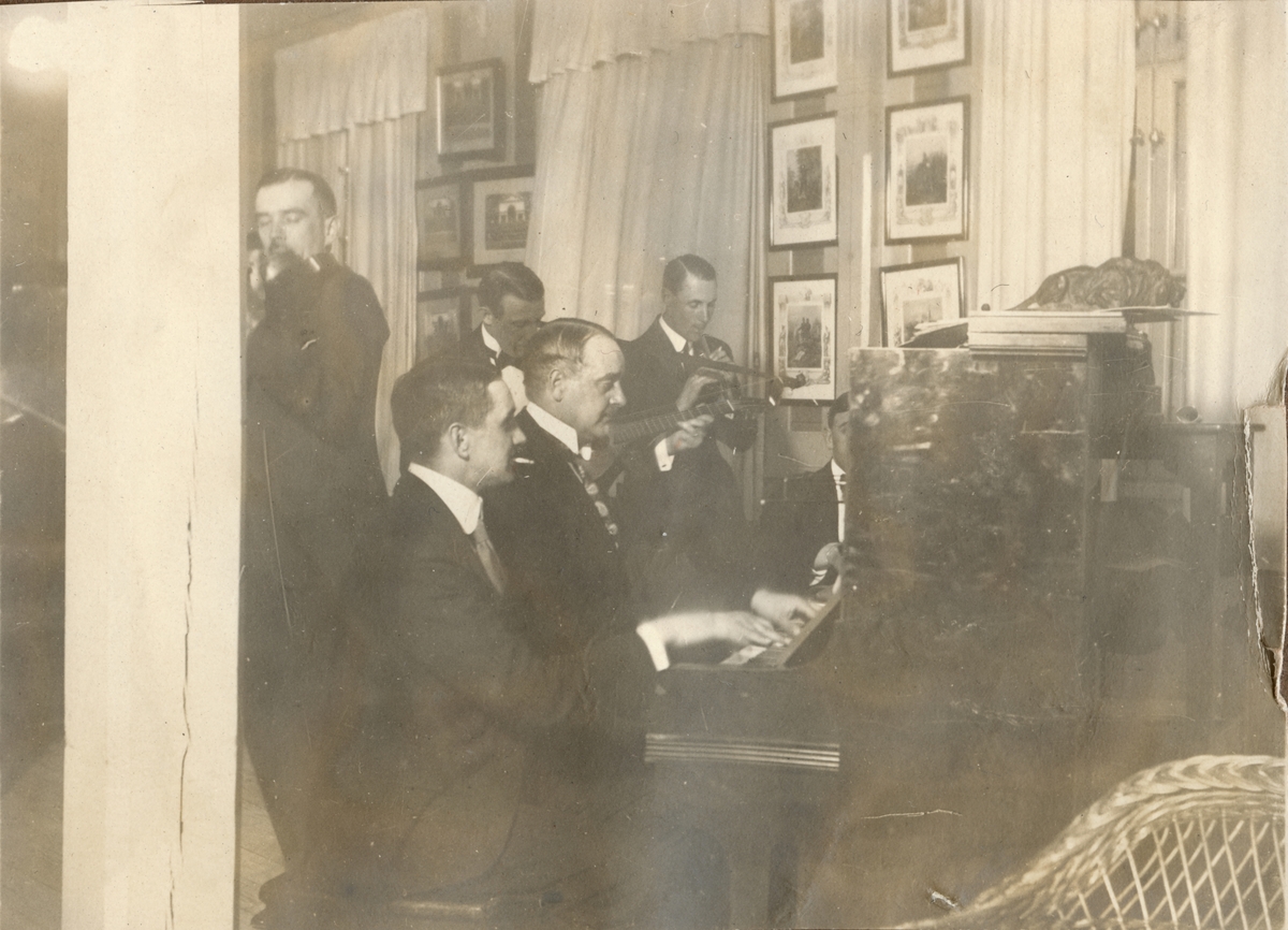 Text i fotoalbum: "Förbindelsekursen 1920". Musicerande män kring piano.