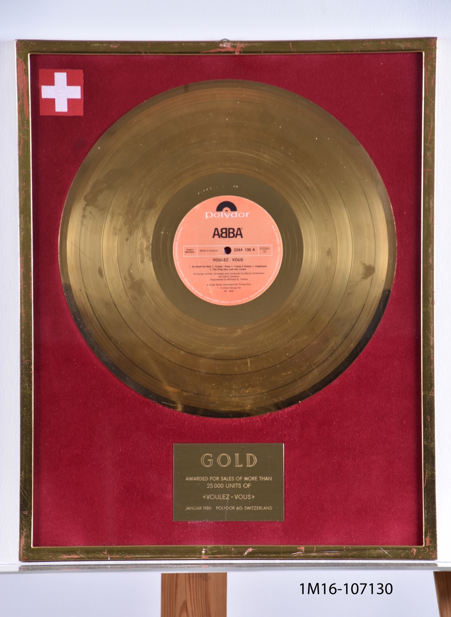 Guldskiva utfärdat för albumet Voulez-Vous för mer än 25 000 sålda enheter. Utfärdat januari 1980 av Plydor AG, Schweiz. Guldskiva mot röd bakgrund. Plakett under skiva. Schweiz flagga i övre vänstra hörnet.