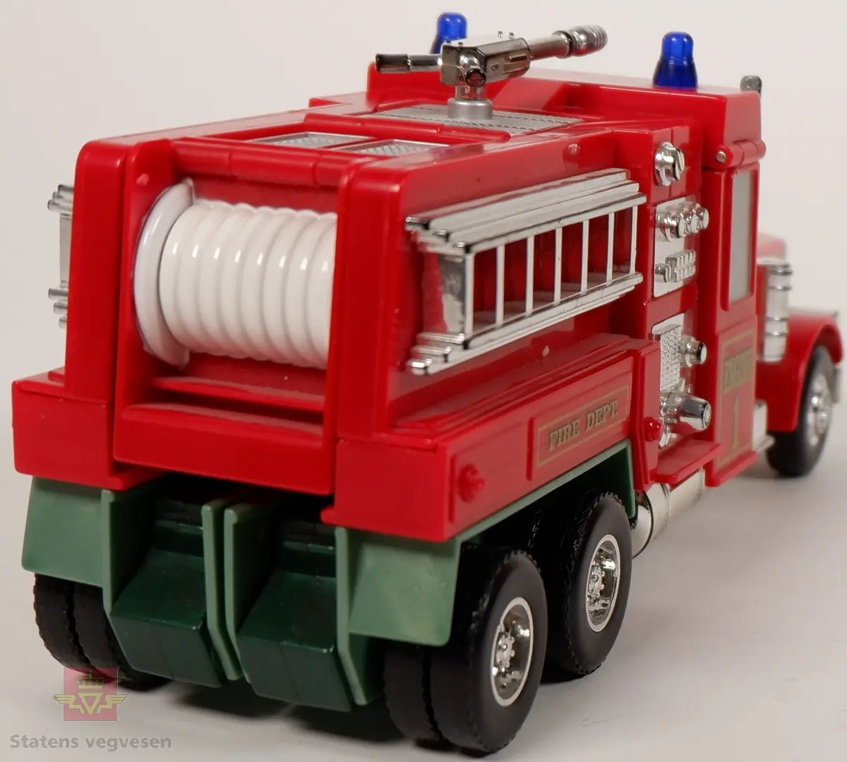 Miniatyrlastebil utformet som brannbil. Lastebilen kan brettes ut slik at det blir en lekefigur. Fargen er rød med påskrifter i gull, detaljer i sølv og to blå blinklamper på taket. Miniatyren er laget av plast og metall.