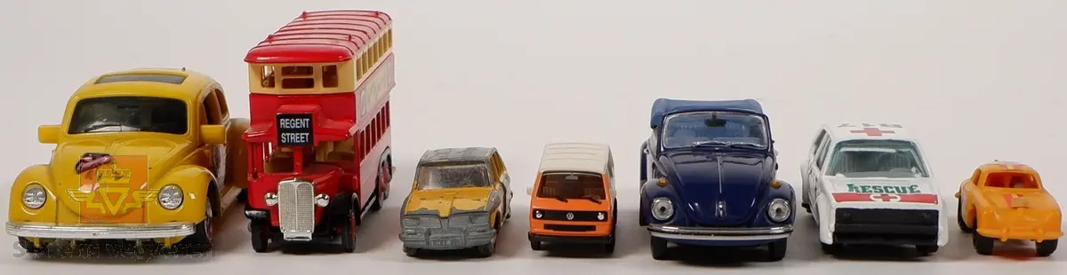 Syv miniatyrmodeller av kjøretøy. En av modellene er utformet som buss, mens resterende seks modeller er utformet som personbiler. Modellene har forskjellige farger og dekoreringer. Hovedfargen på kjøretøyene er hvit, gul, blå, oransje og rød. Fem av modellene er laget i metall, og to er laget i plast. To av modellene er merket med skala, en er merket med 1:66 og en er merket med 1:43.