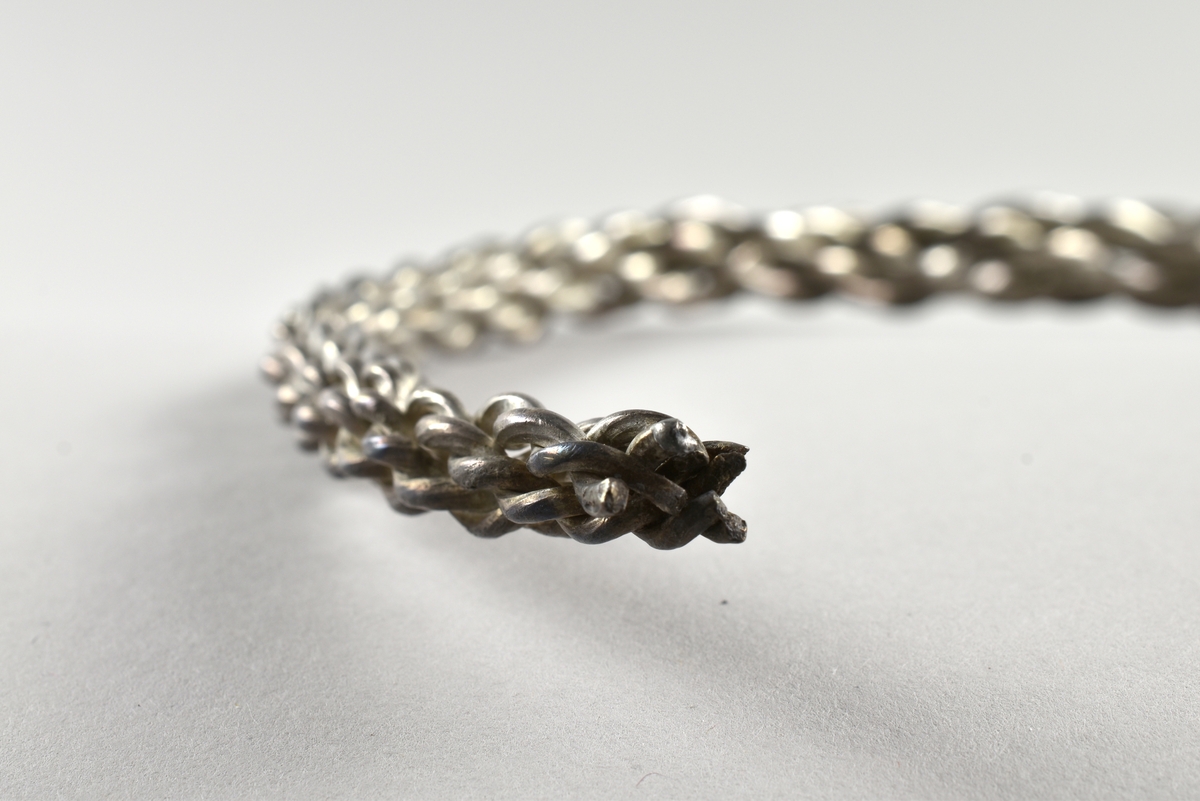 Öppen, stel, halsring av silver från vikingatid.
Tillverkad av åtta tjockare silvertrådar som är sammanflätade. Halsringen är tjockare på mitten och smalnar av mot ändarna.