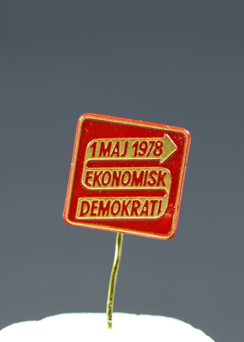Ett fyrkantigt nålmärke i guld och rött med präglad text. Bakgruden är röd och i en guldig pil står "1 maj 1978 Ekonomisk Demokrati". 
Tillstånd vid förvärv: Nålen är något böjd.