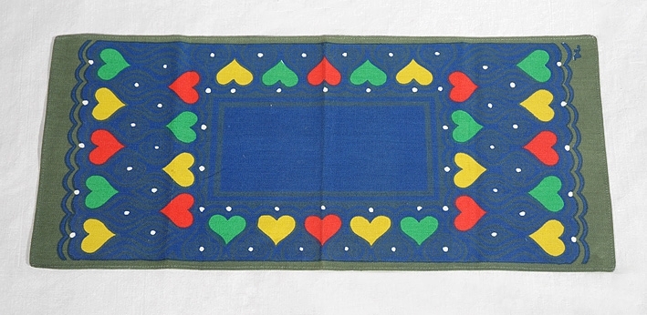 Löpare i grön botten med tryck i rött, gult, vitt, grönt och blått. Trycket föreställer hjärtan och prickar på en blå mönstrad botten. I ena kortsidan tryckta bokstäverna "WL".