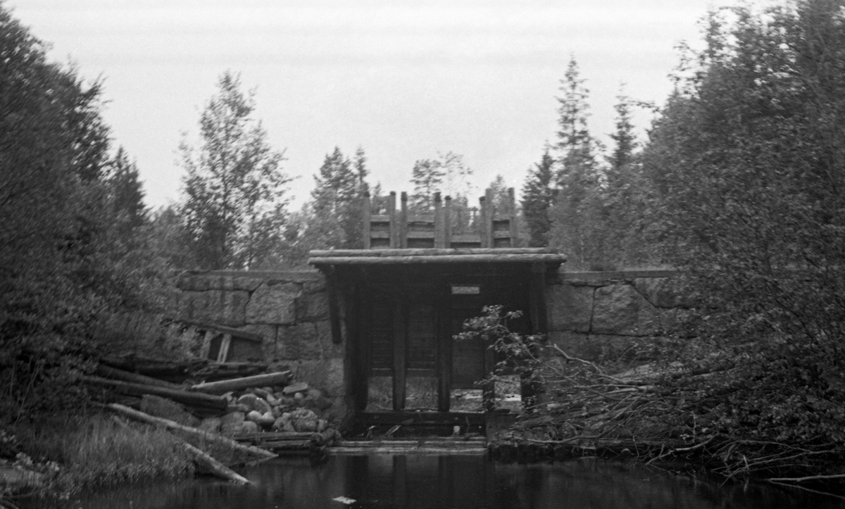 Bergsjødammen, en lukedam i den sørlige delen av Stange kommune i Hedmark, fotografert fra nedsida (i motstrøms retning) en sommerdag i 1955. Det dreier seg om en dam der det ytre skallet er murt av naturstein. Den har ett løp der vannføringa kunne reguleres ved hjelp av fire hev- og senkbare treluker.Da dette fotografiet ble tatt sto lukene opptrukket såpass at vannspeilet i den bakenforliggende dammen må ha vært forholdsvis lavt. 

Bergsjødammen regulerte, som navnet indikerer, Bergsjøen, som 5-6 kilometer sørøst for Espa og omtrent like langt nordøst for Strandlykkja, to tidligere stoppesteder for Dovrebanen langs Mjøsa. Sjøl om avstanden til den store innsjøen er forholdsvis kort, dreneres vannet fra Bergsjøen sørøstover, i første omgang gjennom Bergsjøåa (der dette bildet er tatt) til Hersjøen. Derfra renner vannet videre sørøstover, først under navnet Hersjøåa, etter sammenløpet med Lalumsåa blir vassdraget kalt Knukåa, som etter hvert renner ut i Gjeddevatnet. Fra utløpet av denne innsjøen kalles vassdraget Trautåa, et navn det beholder inntil det renner ut i innsjøen Råsen i Nord-Odal. Vassdraget skal ha vært fløtbart fra det stedet dette fotografiet er tatt.