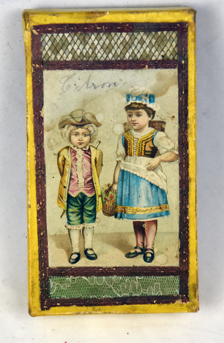 På bildet på lokket er det 2 barn med fine drakter, en jente og en gutt. Jenta har en kurv på ryggen og en kurv i den ene hånden med blomster