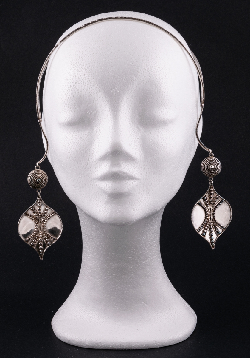 Ashwa, smycke i silver av Rosa Taikon.
Öronsmycke i form av två silverlöv med granalieornamentik, vilka via varsin granelerad kula hänger i en dubbel bygel att sätta över huvudet.
