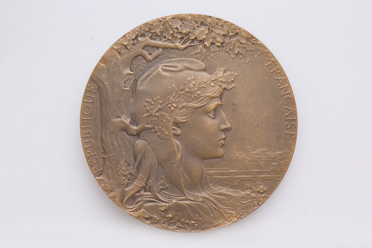Medalje og rødt etui. Den bronsestøpte medaljen med gravert innskripsjon er datert til 1900. Medaljen er produsert i Frankrike og er en pris gitt på utstilling.