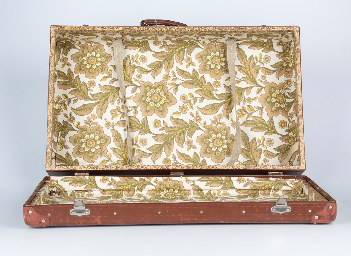 Koffert med lærhåndtak og bakelittforsterkede hjørner. Innvendig blomstermønstret papirfor.