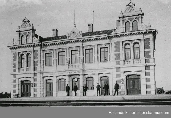Falkenbergs järnvägsstation. Stationen tillkom i samband med Mellersta Hallands järnväg som invigdes 1886 och gick mellan Varberg-Halmstad. På perrongen står sex män som ser ut att vara uniformerade såsom stationspersonal.
