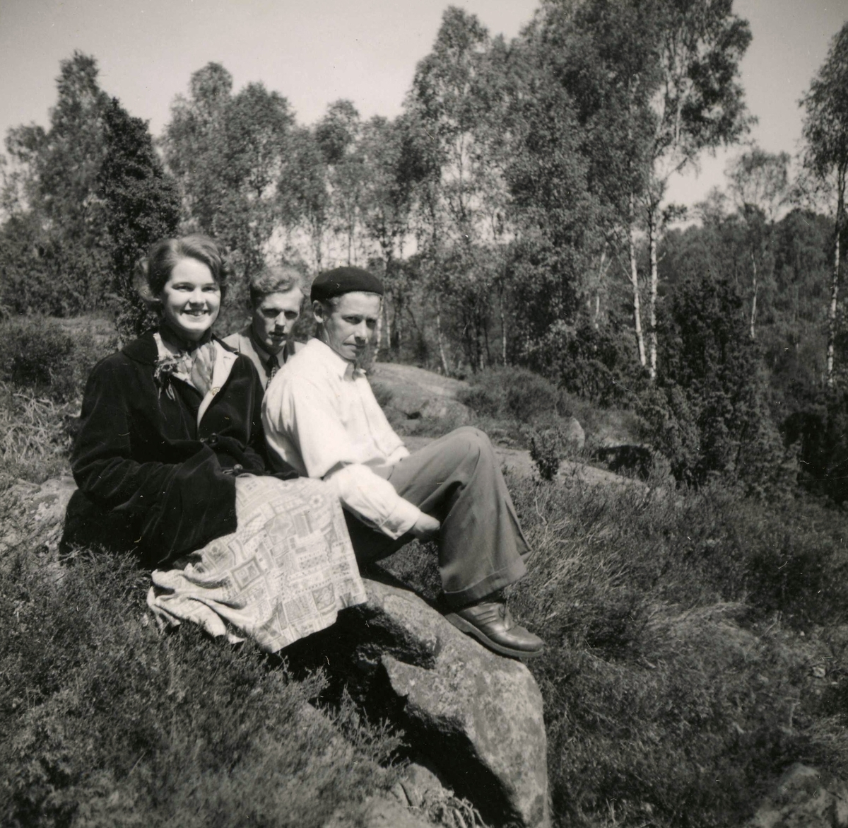Tre personer sitter på en stenbumling vid Ekans gård, Ekan 1:1 år 1953. Från vänster: 1. Eva Svensson (född 1936, gift Johansson), Ekan. 2. Sven Erik Stenbom (1926 - 2003), Tollered. 3. (Evas far i basker) Rolf Svensson (1909 - 1989), Ekan. Tollered var en granngård till Ekan.