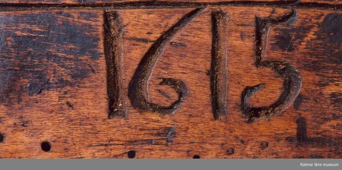 KLM 2100. Låda av trä. Fyrkantig, skjutlock med grova ornament. Skuren i ett stycke. På ena sidan: 1615, på den andra E.L. På locket inristat en månguddig stjärna. Okänd användning.